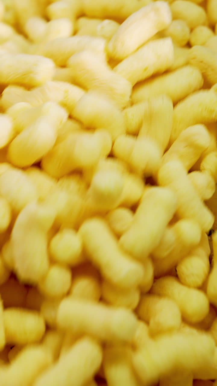 Crunchy yellow puffcorn moving on the conveyor. Crispy corn snacks producing. Vertical video