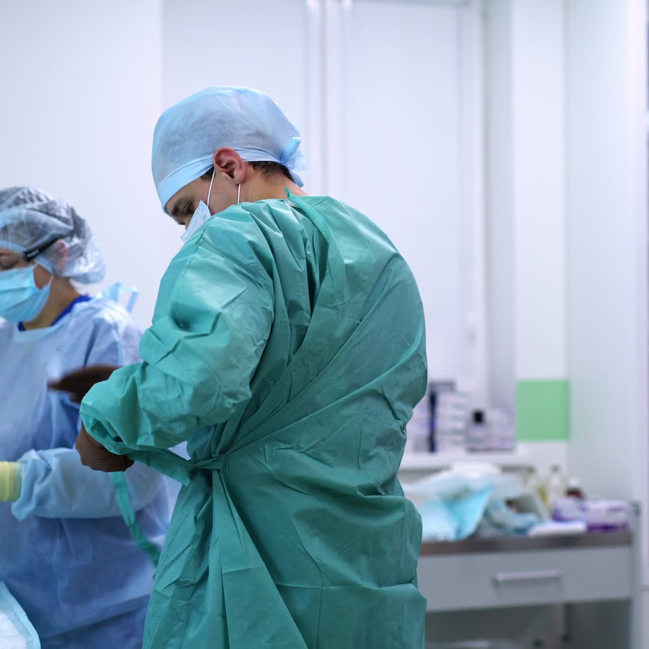 Young male surgeon getting dressed for operation. Female nurse helping the doctor to put on gloves and coat