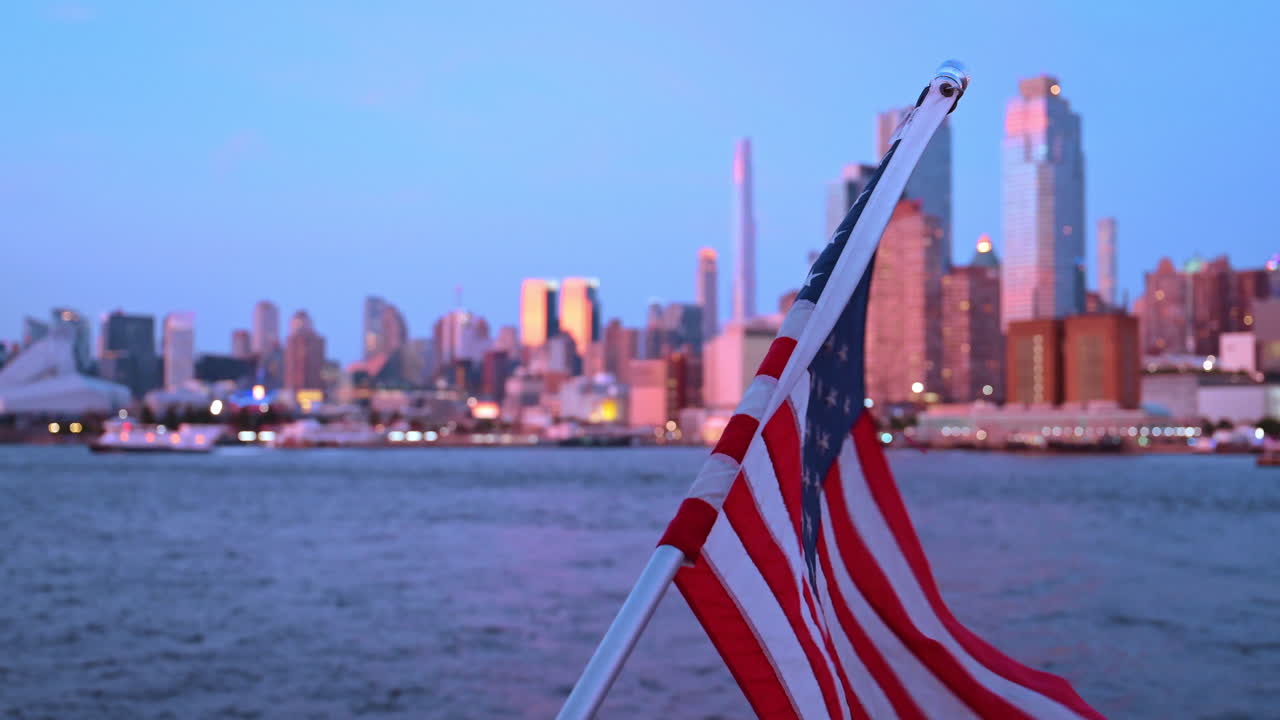View of New York skyline with American flag by the water at dusk. A flag waves by the water with New York's skyline in the background
