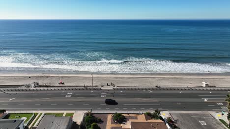 aerial from left to right of the beautiful beach in carlsbad california, usa and coast highway with cars passing by beside the beach on a town landscape