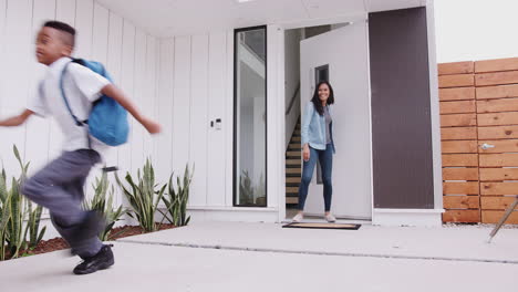 Excited-Children-Running-Out-Of-Front-Door-On-Way-To-School-Watched-By-Mother