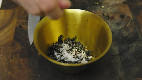 chef adding grains of salt into bowl with seaweed