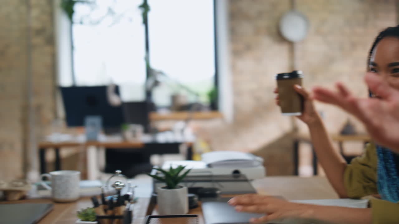 Startupper sorridenti che si divertono durante la pausa caffè seduti al tavolo dell'ufficio, primo piano.