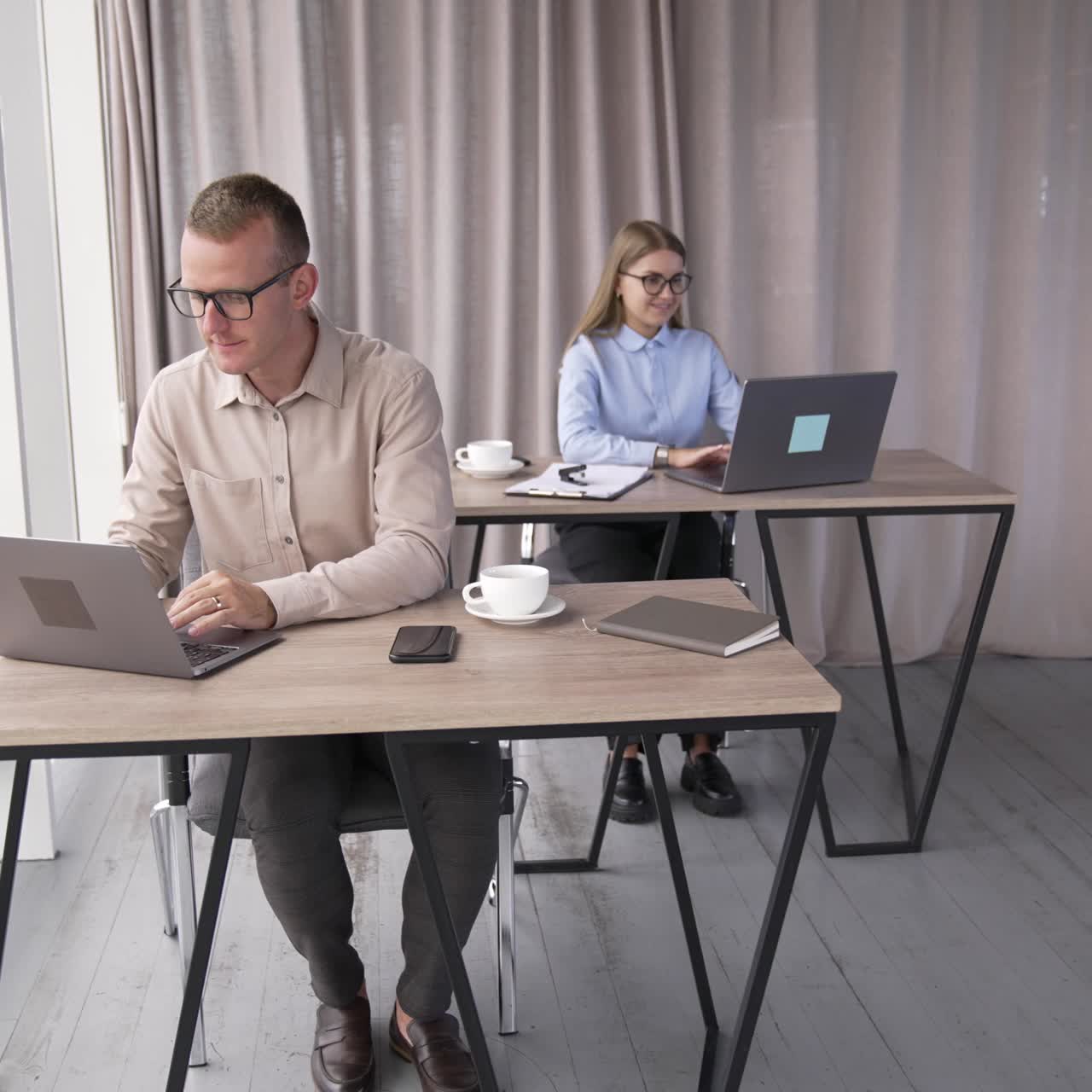 Young mid-aged teammates working in the office sitting in front of laptops. Portrait of a male employee wearing glasses close up