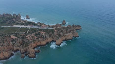 Szenischer-Hintergrund-Luftdrohnenansicht-Der-Felsigen-Küste-Von-Lagos-Mit-Leuchtturm-Am-Rand,-Portugal,-Vorwärts-Fliegend,-Tag