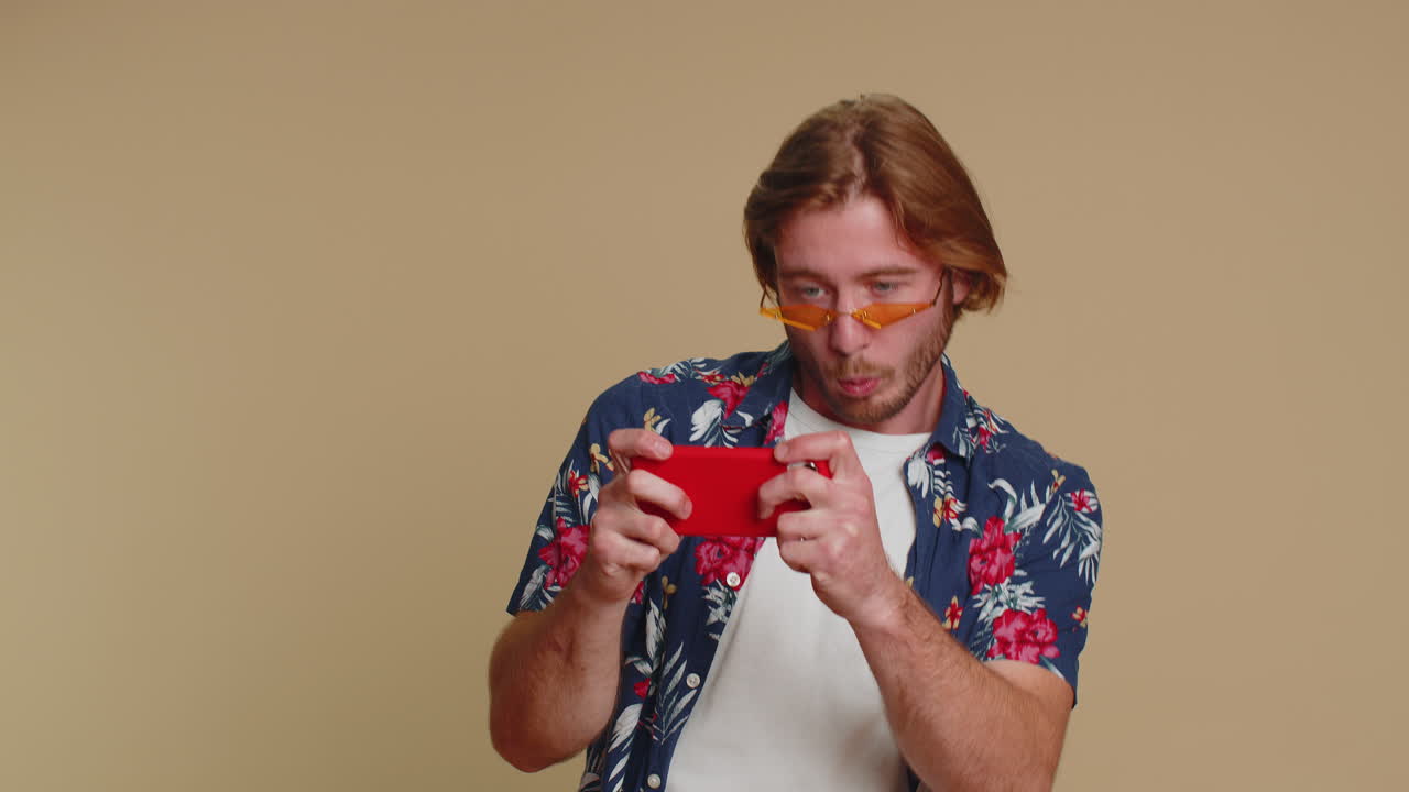 un turista adicto y divertido, preocupado, jugando con entusiasmo a videojuegos de carreras en su teléfono móvil