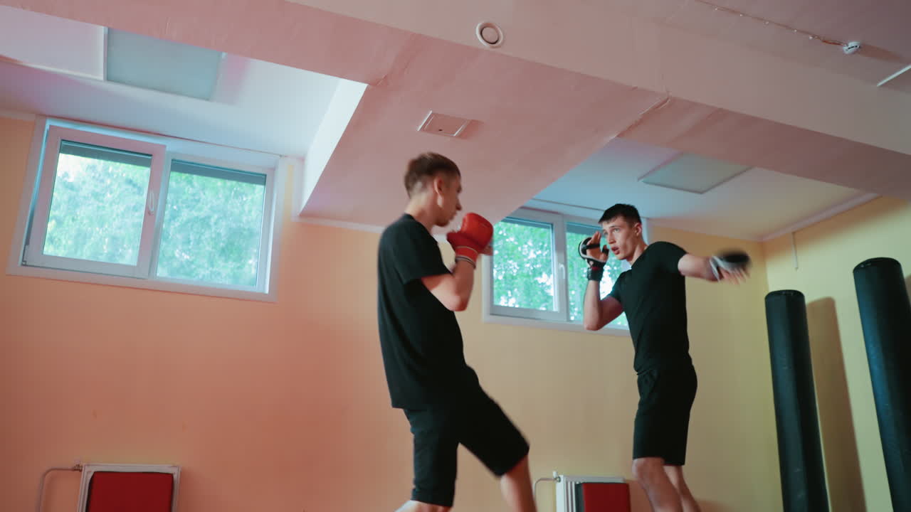 Wrestlers in black sportswear practice sparring inside gym with red floor and padded walls, wearing gloves while training defense and offense techniques during intense match