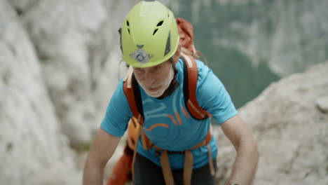 a hiker climbing up a mountain, wearing light green helmet, blue t-shirt and an orange backpack