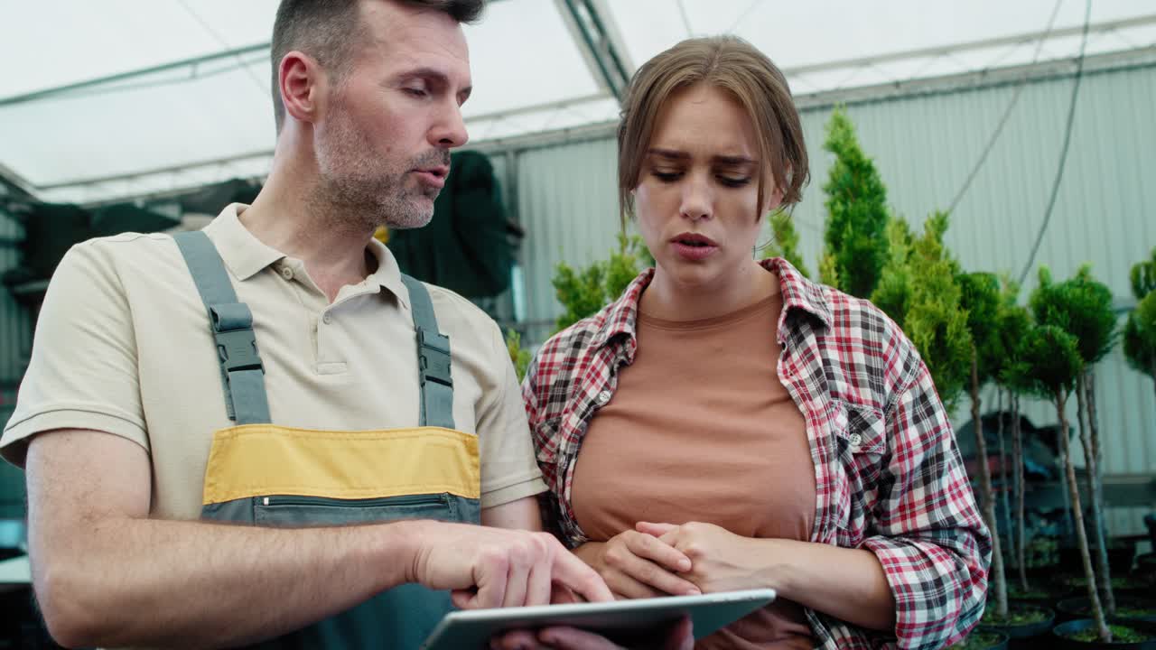 Close up of two caucasian botanists working in greenhouse and using tablet