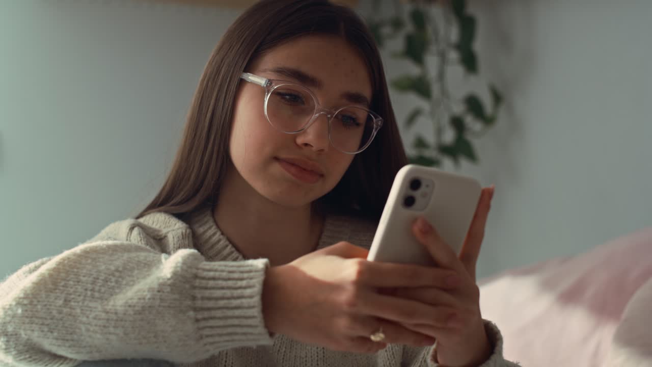 primer plano de una adolescente caucásica navegando por el teléfono en su dormitorio