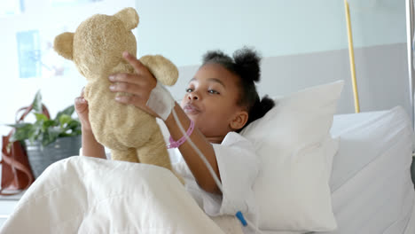 happy african american girl playing with mascot in hospital bed, slow motion