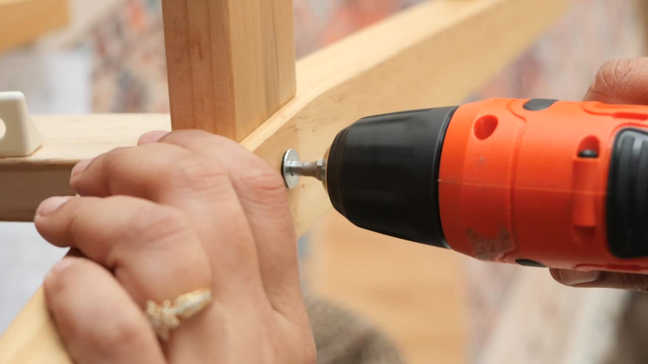 Close-up of a person using a power drill to insert a screw into wood