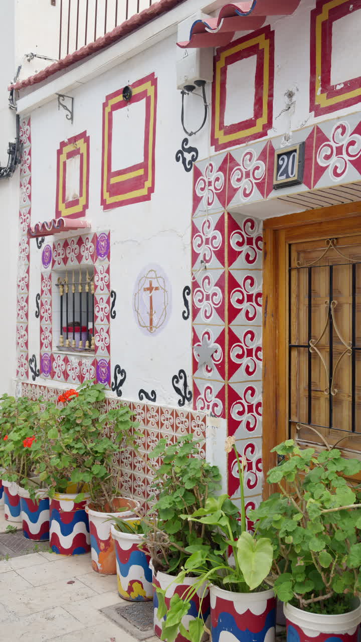 Alicante, Spain - May 30, 2025: Close up of a traditional house in Barrio de Santa Cruz, decorated with colorful painted tiles, potted plants, and a wooden door. Vertical