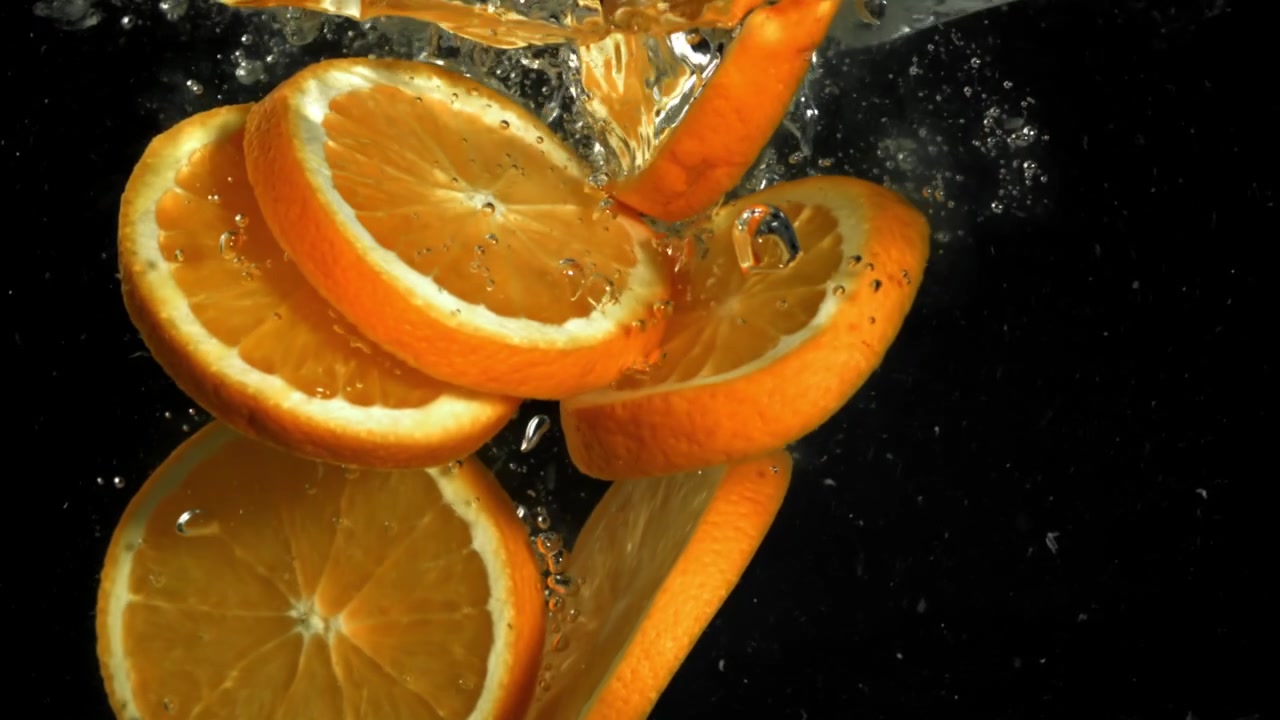 Fette d'arancia che cadono al rallentatore nell'acqua con bolle.