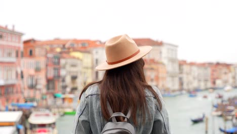 vrouw keert terug om naar het grand canal van venetië te kijken en neemt haar hoed af.