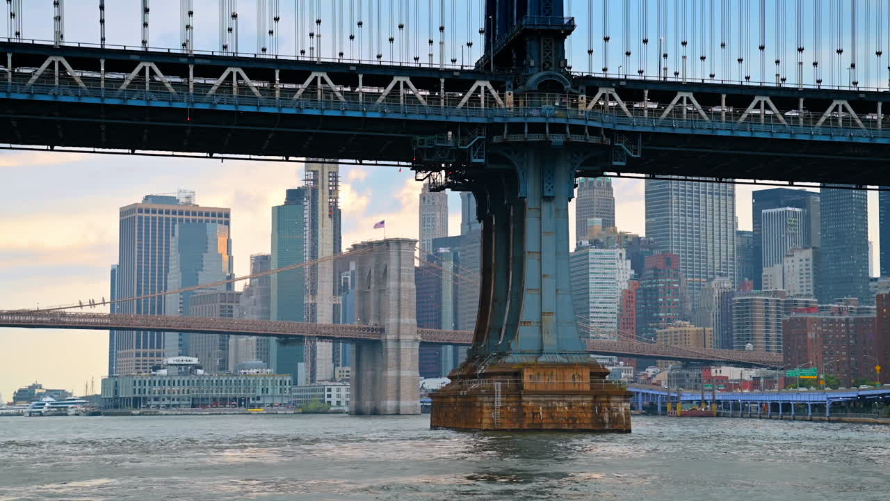 View on the support of the Manhattan Bridge from the riverscape. The Brooklyn Bridge and New York skyline at backdrop