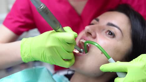 Dentist-cleans-woman's-teeth-with-professional-toothpaste-and-automatic-brush.-Dentist-using-saliva-ejector-or-dental-pump-to-evacuate-saliva.