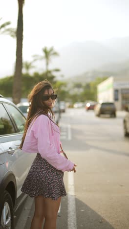 young woman in a pink blouse and floral skirt near a parked car