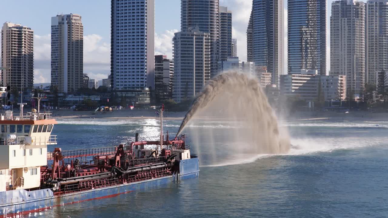 A dredger pumps sand in Gold Coast waters, set against a backdrop of skyscrapers under clear daylight