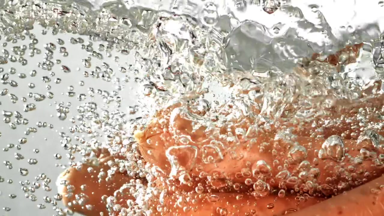 Salsicce che cadono nell'acqua bollente con bolle, al rallentatore.