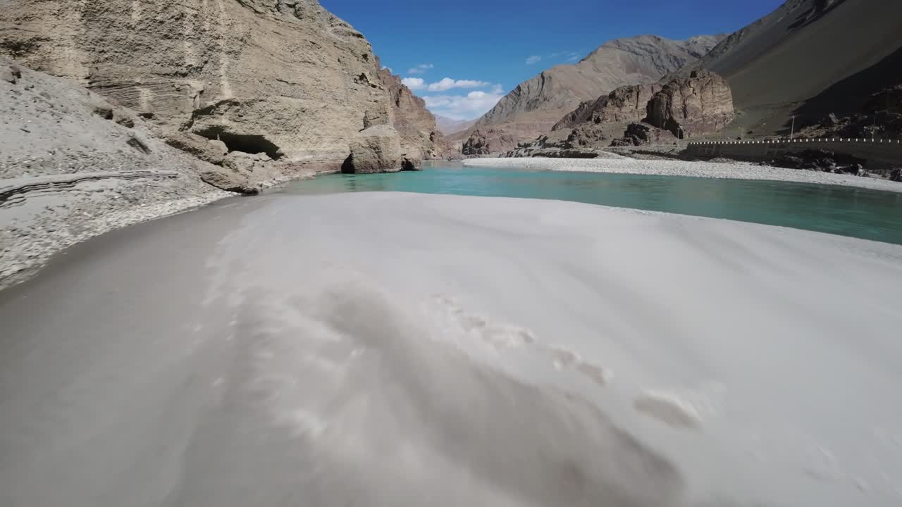 Il fiume Indo scorre attraverso una valle ad alta quota in Ladakh, India, con acqua turchese delimitata da terreno roccioso e montagne brulle. Un volo FPV a bassa quota segue da vicino la riva del fiume.