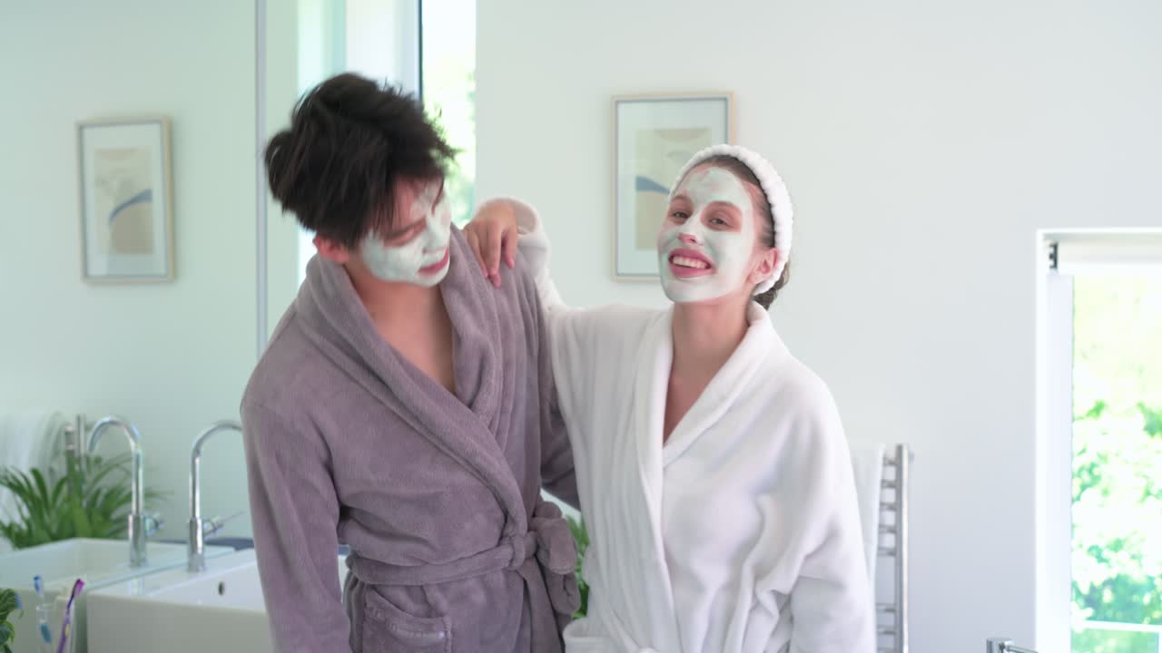 Couple sharing masks, woman placing arm on man's shoulder, leaning and laughing in bathroom