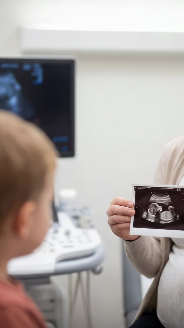 Vertical video: Holding sonogram print after scan in clinic, mom in cardigan showing baby to child