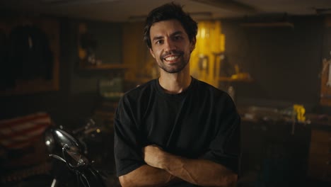 Portrait-of-a-happy-brunette-guy-with-stubble-in-a-gray-T-shirt-who-is-posing-from-his-workshop-studio