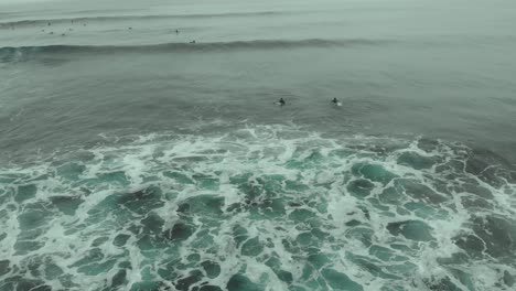Aerial-orbit-around-Surfers-swimming-at-the-sea,-Pichilemu,-Chile