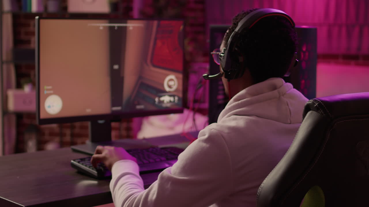 Over shoulder view of african american gamer using pc gaming setup relaxing playing first person shoote