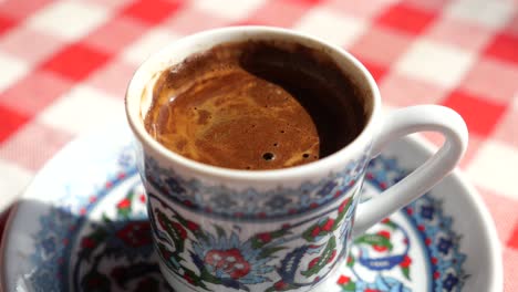 close up of a cup of traditional turkish coffee on a red and white tablecloth