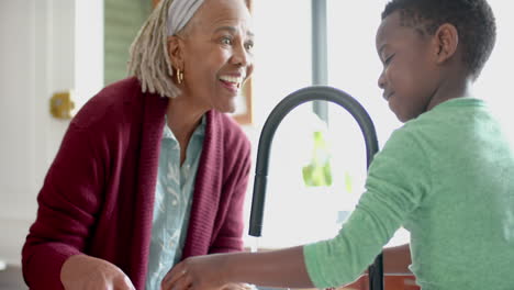 Happy-african-american-grandmother-and-grandson-washing-vegetables-in-kitchen,-slow-motion