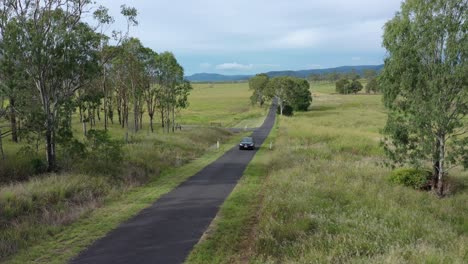 Drone-shot-tracking-car-driving-along-country-road,-stationary-camera