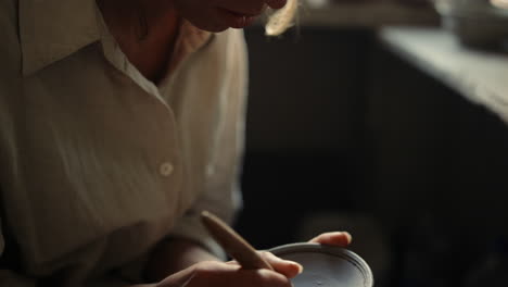 Young-woman-drawing-ornament-on-clay-plate-in-pottery.-Girl-carving-on-wet-clay