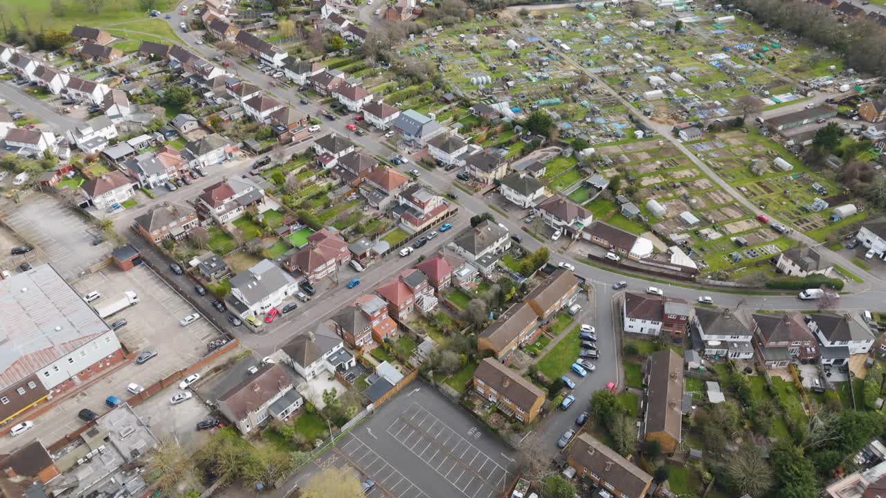 Aerial view of British suburban street lined with terraced and semi-detached houses backing onto neatly partitioned allotments alive with greenhouses, sheds and flourishing vegetable plots