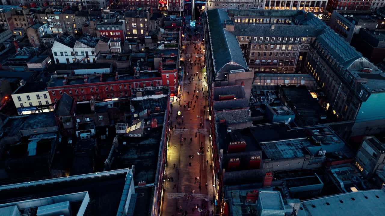aerial landscape drone shot flying over O'Connell street in Dublin Ireland at twilight blue hour in winter with birds flying and tourists walking around below the busy lit street and Irish buildings