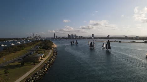 fleet of sailing boats racing towards a urban skyline rising above a city harbor