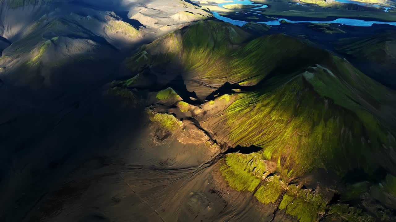 Cinematic aerial establishing shot of Iceland’s volcanic highlands, showing rugged moss-covered peaks, deep shadows and distant lakes under crisp atmospheric light