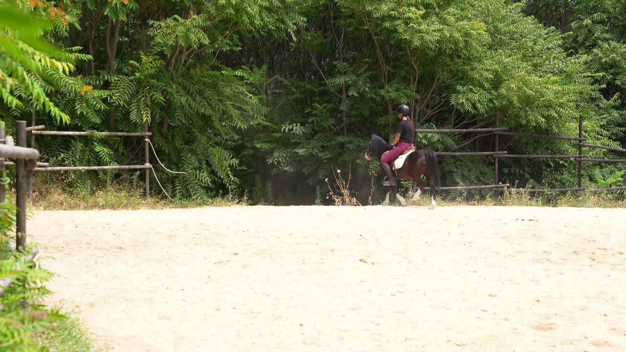 Distant rear view of a helmeted woman riding a pony away from the track after a training session
