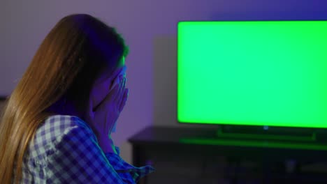 young woman sits on an armchair and watches tv. remote controller