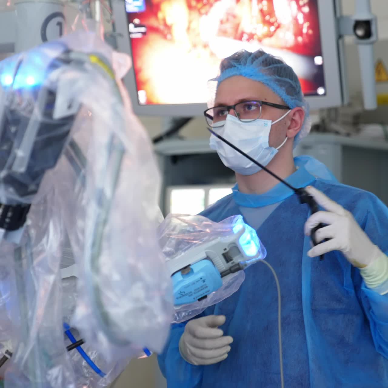 Focused young male surgeon operating the patient with the help of robotic high-precise equipment. Da Vinci robot operating patient. Screen with inner organs at backdrop