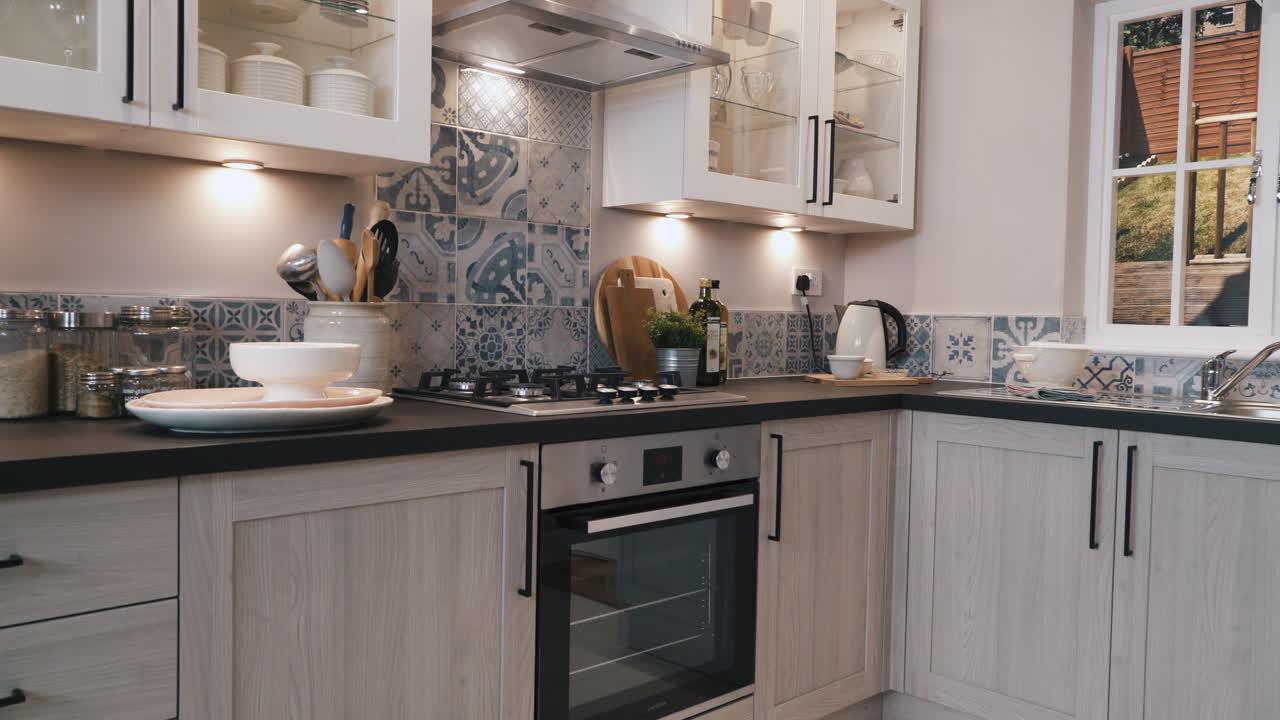 Interno cucina con paraschizzi e piastrelle a fantasia blu, pensili a vista con finiture bianche e ante di armadietti in legno grigio chiaro