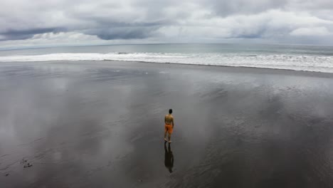 aerial of young man making a round off backflip on an empty beach, colombia