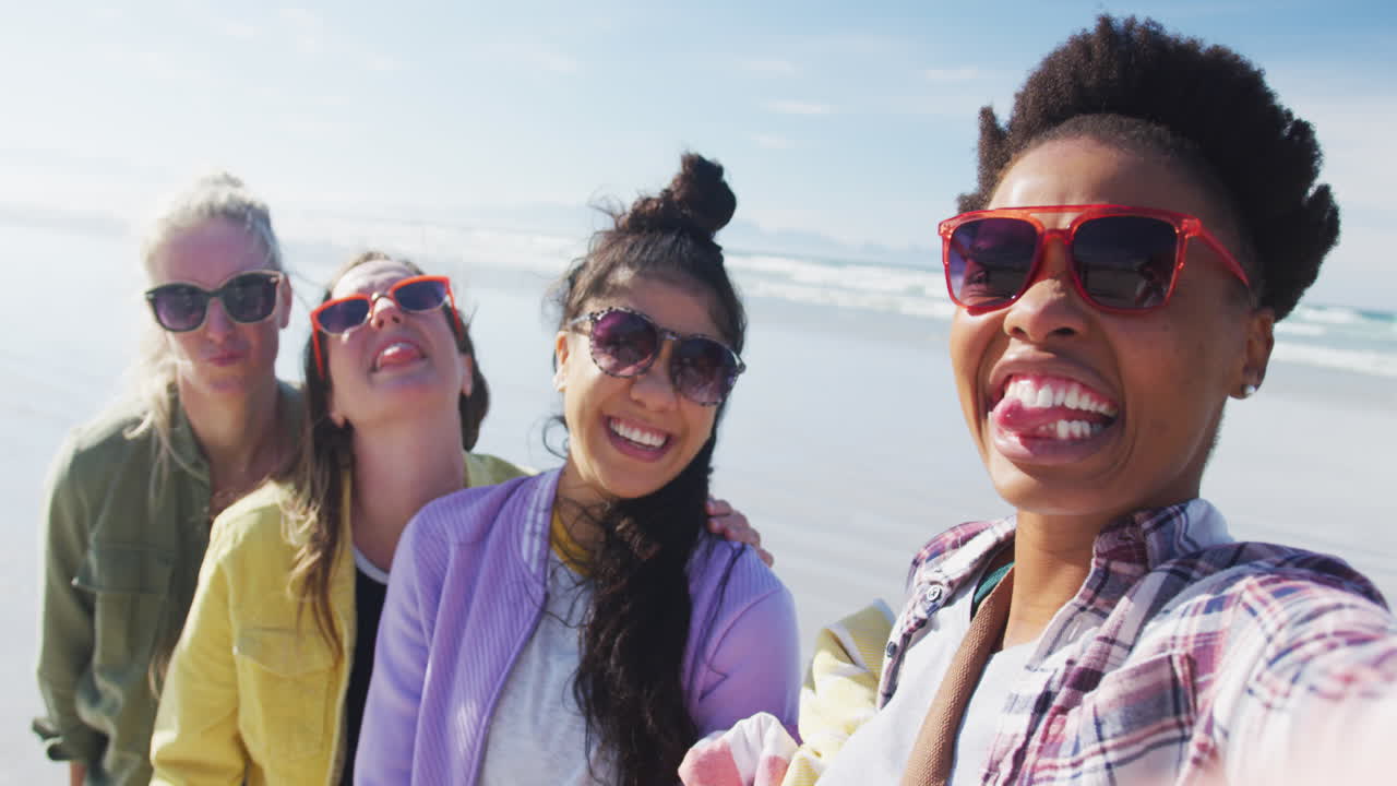 Happy group of diverse female friends having fun, taking selfie with smartphone at the beach