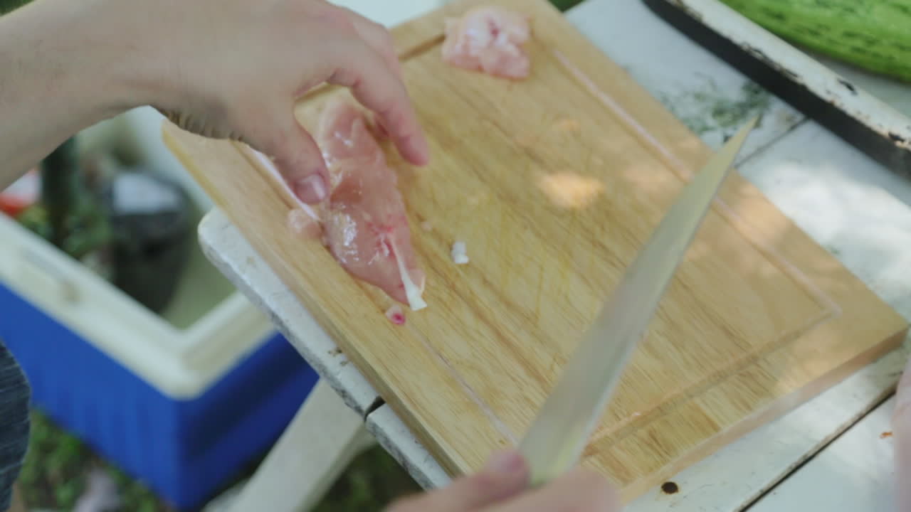 cerca de la mano masculina cortando pollo en la tabla de cortar en la mesa de campamento