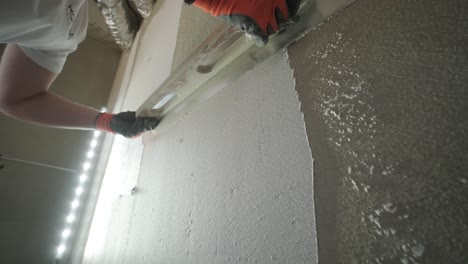 a worker's hand skillfully applies a layer of plaster using a trowel on a wall under bright led lights, showcasing detailed construction work