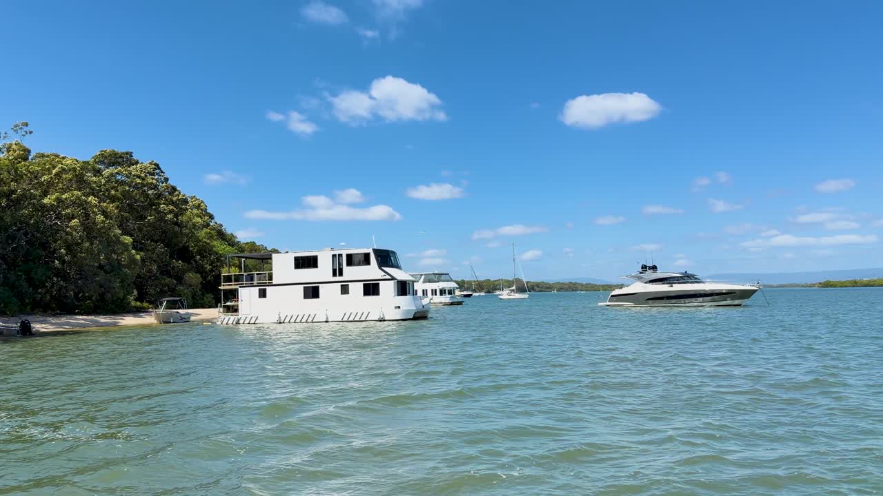 Campo lungo di una casa galleggiante bianca e uno yacht ancorati in acque costiere blu calme