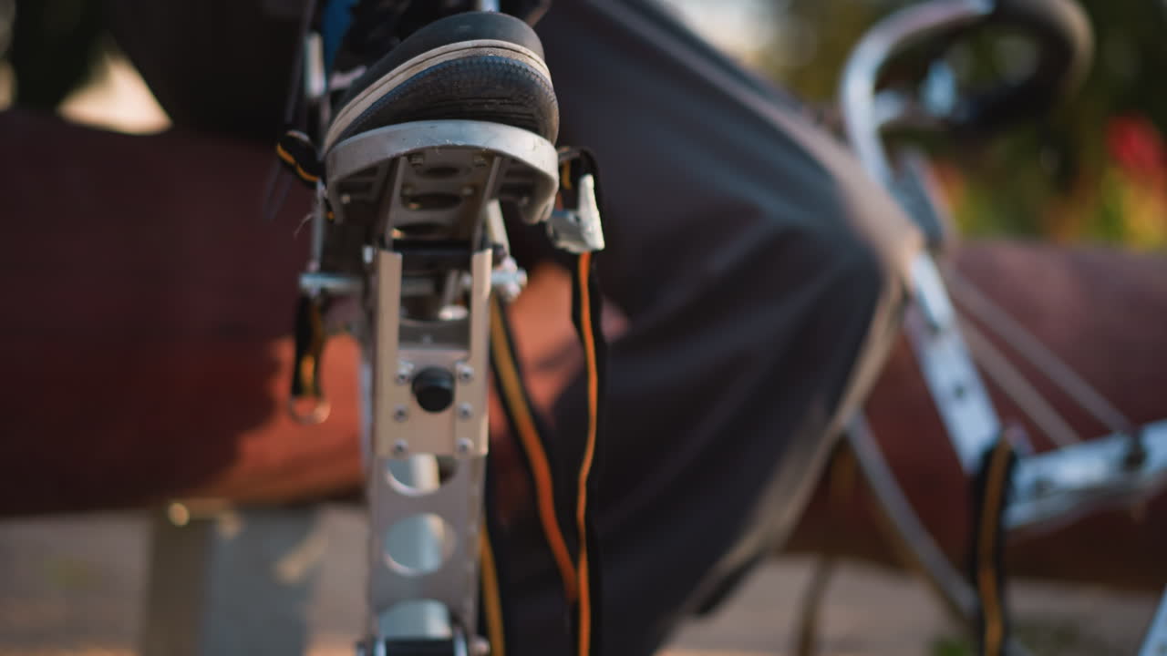 primer plano de los pies del tipo en zapatillas de deporte negras y azules, posicionados en equipos de tiro con arco al aire libre. lleva pantalones oscuros, levantando el equipo ligeramente en luz natural, con vegetación borrosa en el fondo