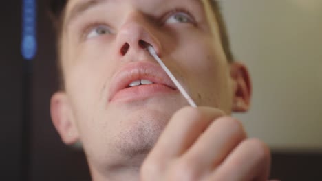 hombre girando un hisopo nasal estéril alrededor de su fosa nasal, kit de prueba covid-19 en casa