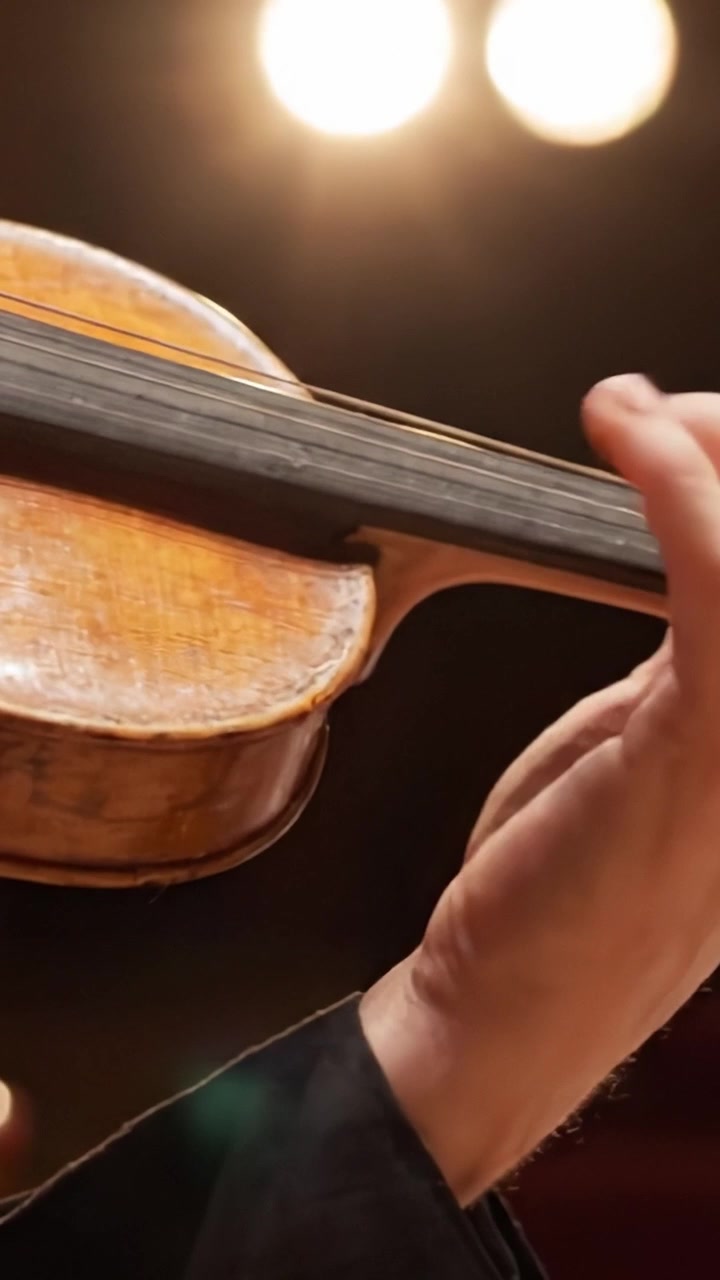 Una vista ravvicinata della mano di un abile violinista che suona con grazia un violino splendidamente realizzato sotto le luci soffuse del palco, catturando l'essenza dell'arte musicale